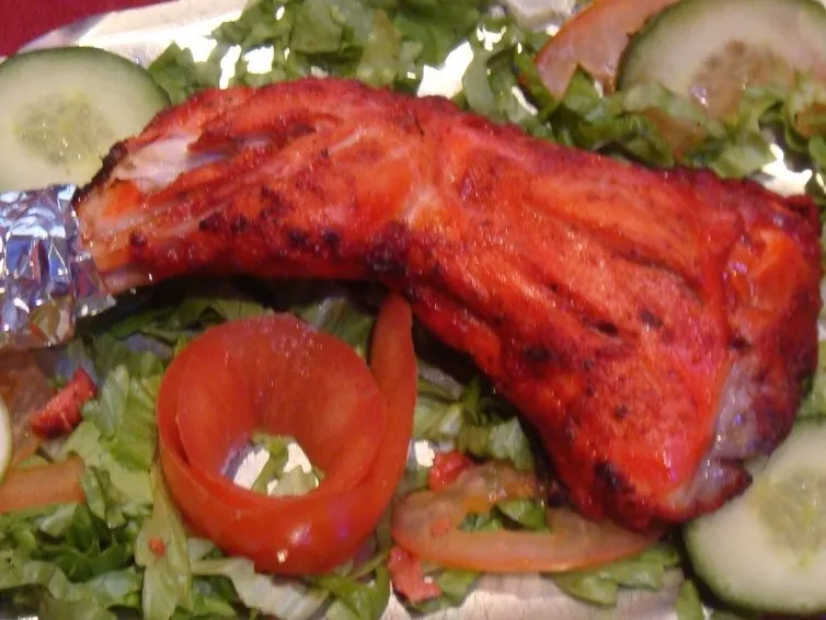 Poulet tandoori grillé, servi sur un lit de salade avec tomate et concombre.